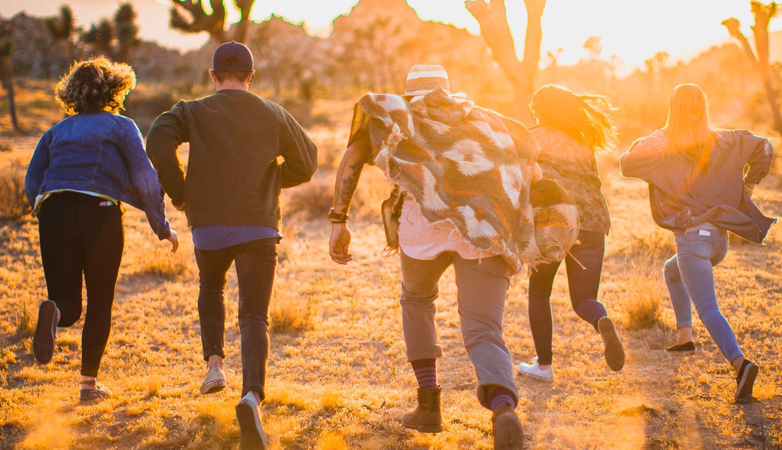 Gruppo di giovani che corre insieme in un paesaggio desertico al tramonto