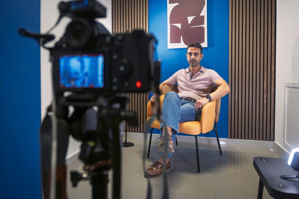 Uomo intervistato seduto su una poltrona davanti a una videocamera
