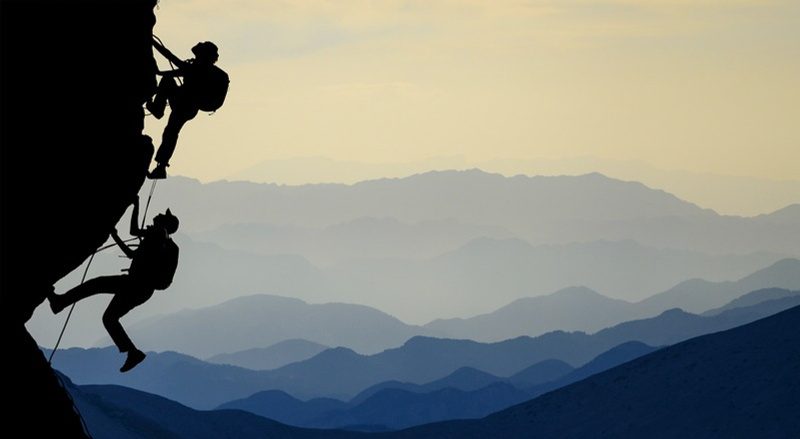 Due arrampicatori in silhouette su una parete con montagne sullo sfondo