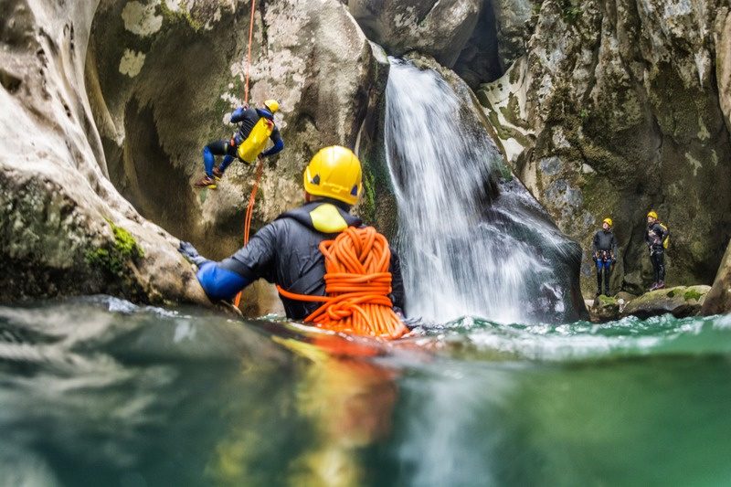 Esploratori con casco e imbracatura in un torrente vicino a una cascata, canyoning