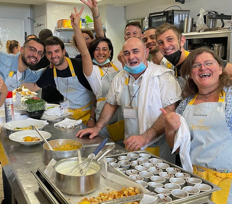 Team sorridente con grembiuli in cucina durante una cooking experience