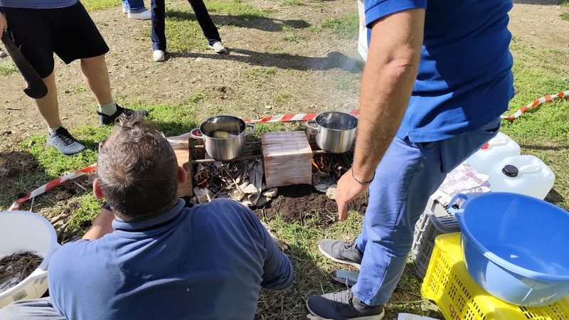 Persone intorno a un fuoco da campo con pentole durante una sfida di gruppo all'aperto