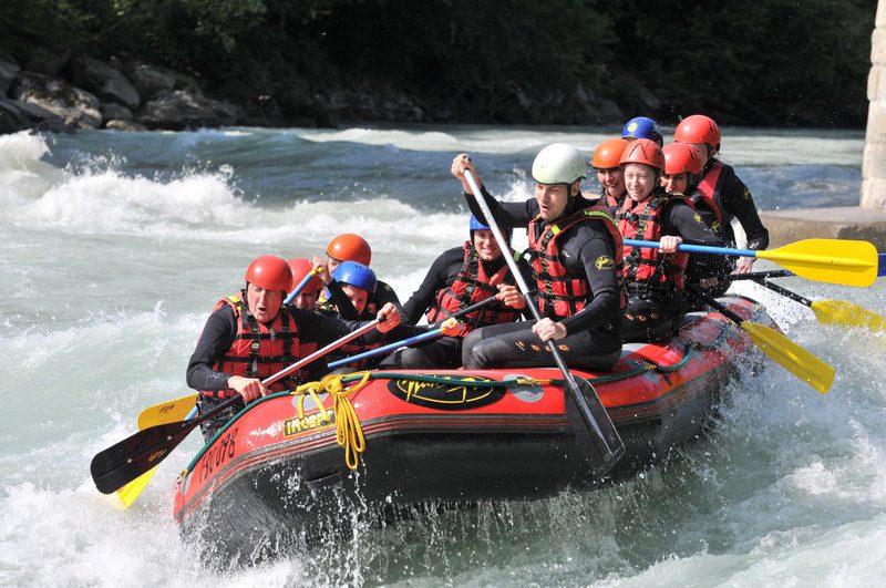 Squadra con caschi e giubbotti su un gommone durante il rafting tra le rapide