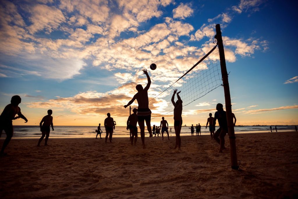 Persone che giocano a beach volley in spiaggia al tramonto