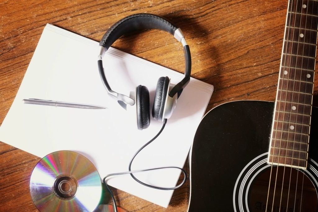 Cuffie, chitarra, taccuino e CD su un tavolo di legno