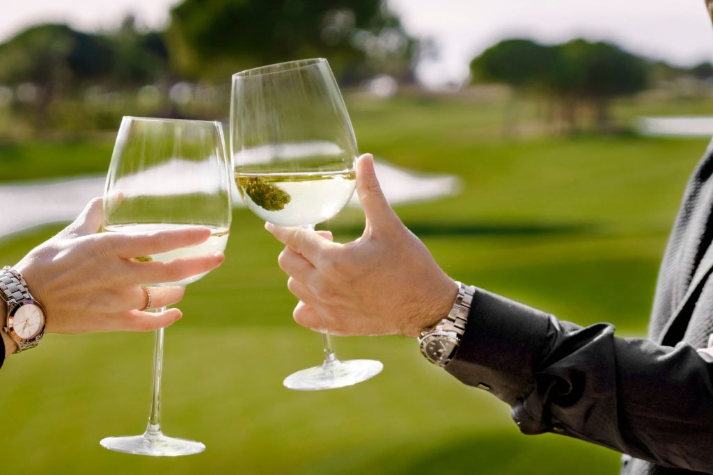 Due persone brindano con un calice di vino bianco su un campo da golf